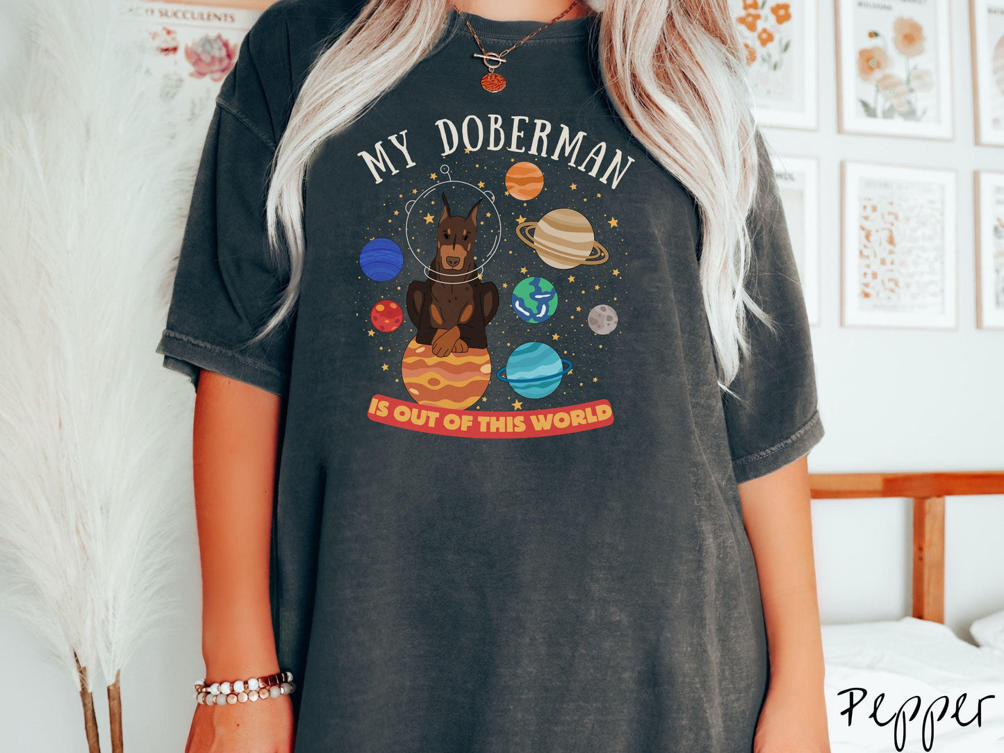 A vintage Comfort Colors t-shirt featuring the text My Doberman is Out of This World. The design showcases a Doberman sitting proudly atop Jupiter, surrounded by a vibrant solar system filled with colorful planets and twinkling stars.