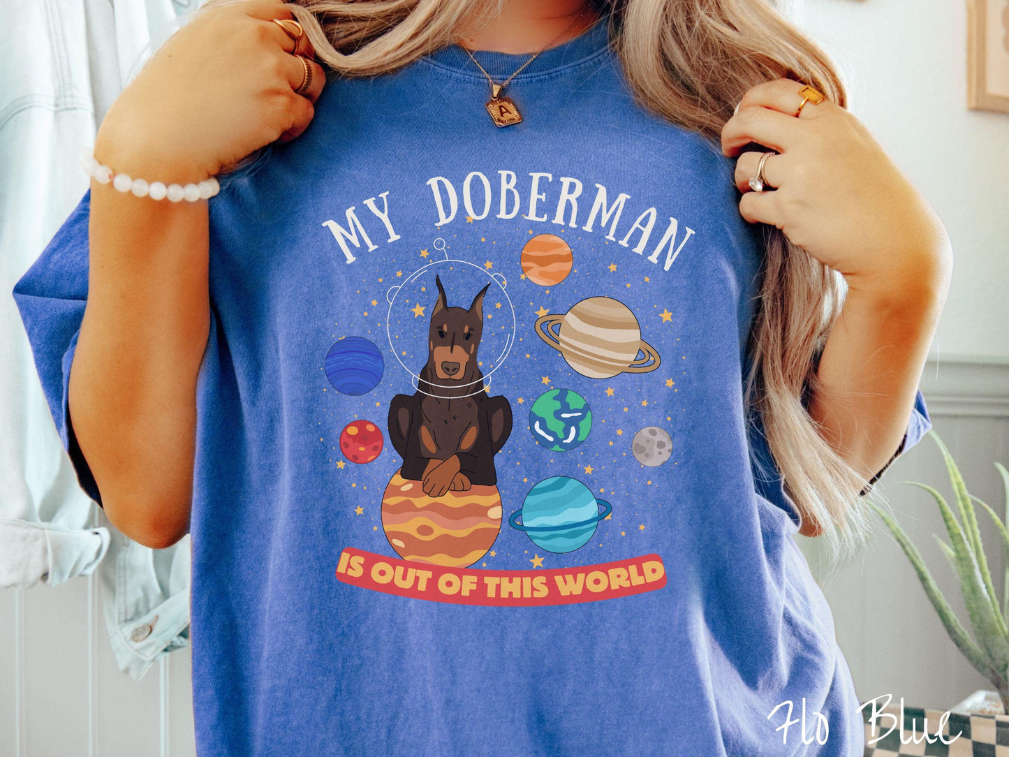 A vintage Comfort Colors t-shirt featuring the text My Doberman is Out of This World. The design showcases a Doberman sitting proudly atop Jupiter, surrounded by a vibrant solar system filled with colorful planets and twinkling stars.