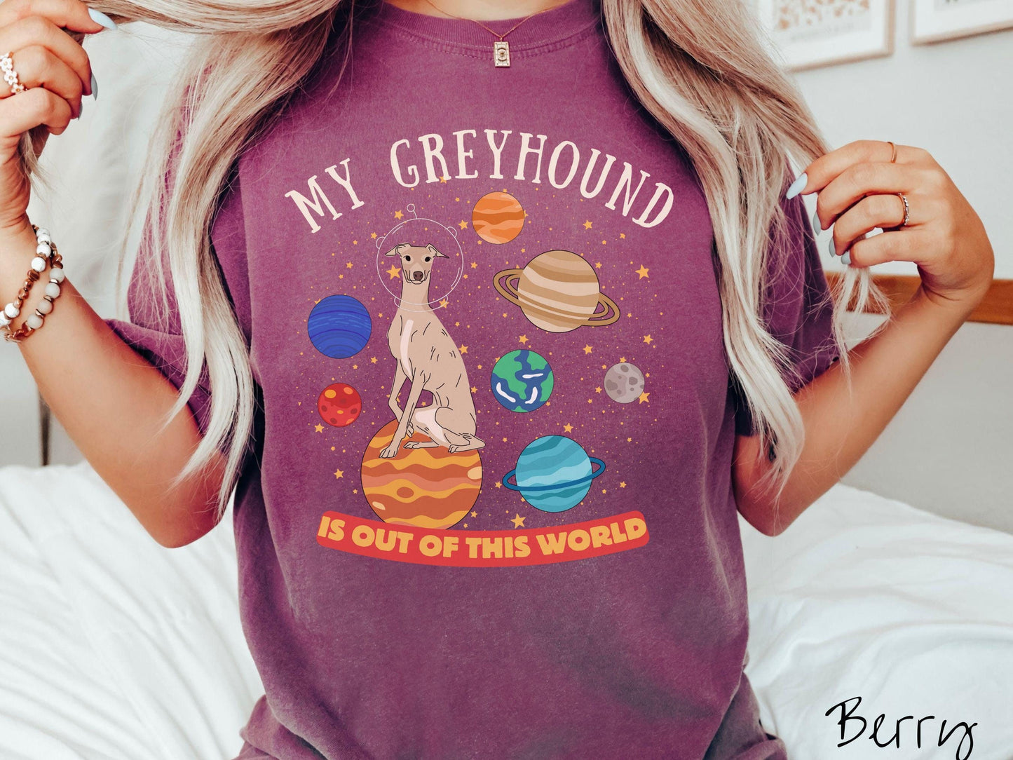 A vintage Comfort Colors t-shirt featuring the text My Greyhound is Out of This World. The design showcases a Greyhound sitting proudly atop Jupiter, surrounded by a vibrant solar system filled with colorful planets and twinkling stars.