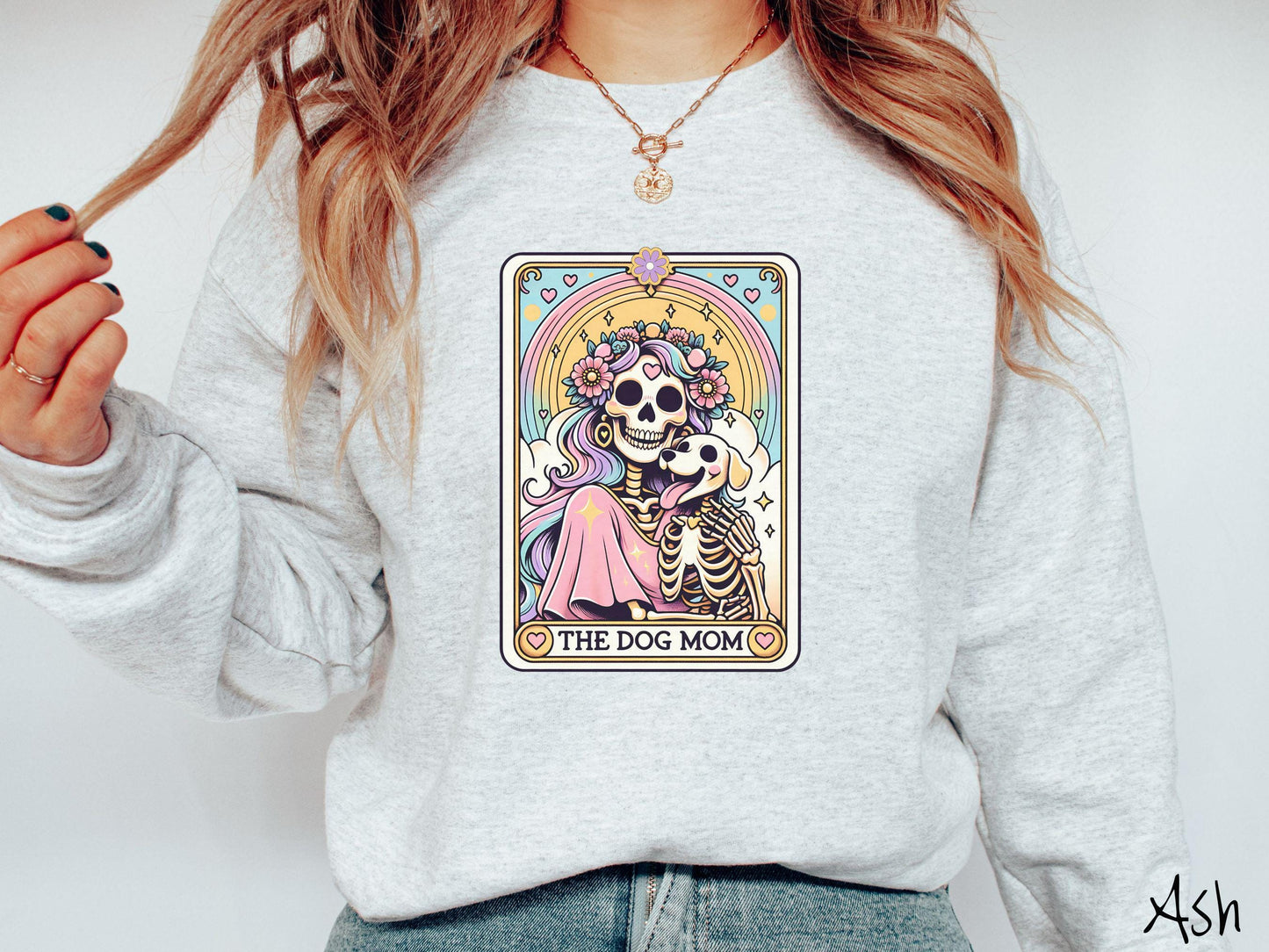 A vintage Gildan sweatshirt features a tarot card design with the text “The Dog Mom” along the bottom, framed by red hearts. Inside the tarot card is a female skeleton with flowing hair adorned with colorful flowers holding a skeleton dog.