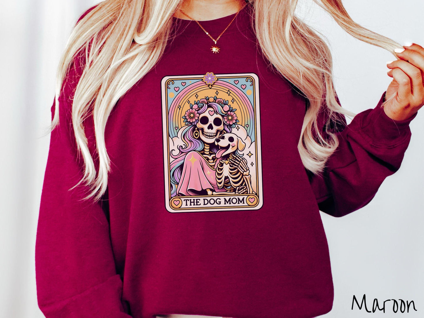 A vintage Gildan sweatshirt features a tarot card design with the text “The Dog Mom” along the bottom, framed by red hearts. Inside the tarot card is a female skeleton with flowing hair adorned with colorful flowers holding a skeleton dog.