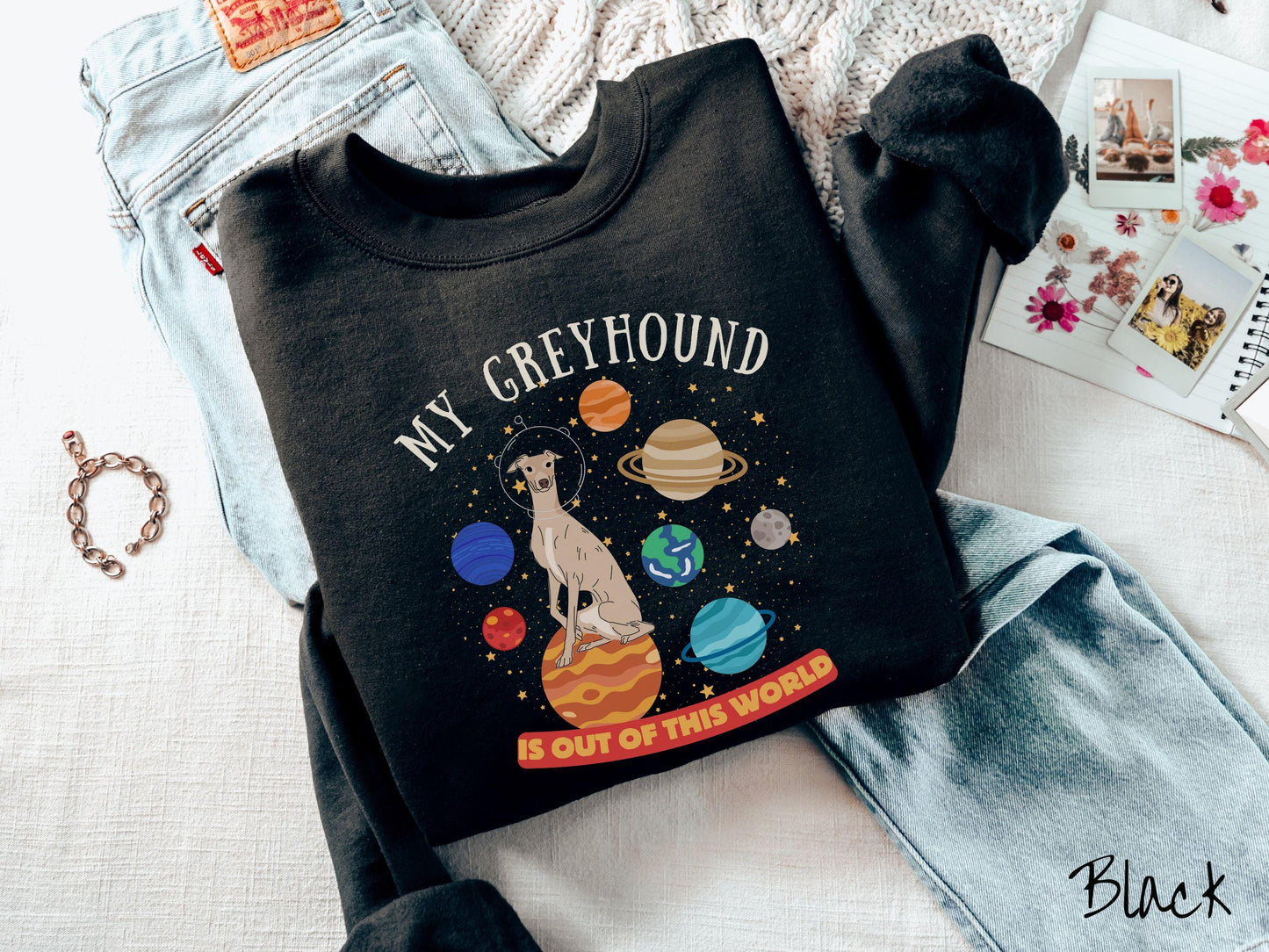 A vintage Gildan sweatshirt featuring the text My Greyhound is Out of This World. The design showcases a Greyhound sitting proudly atop Jupiter, surrounded by a vibrant solar system filled with colorful planets and twinkling stars.