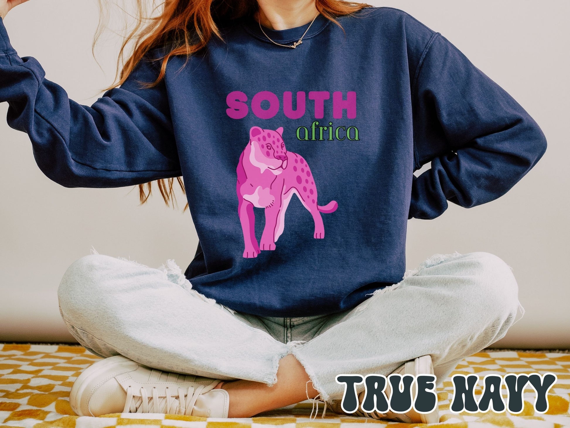 A woman wearing a vintage, true navy colored sweatshirt with the text South Africa in pink and green font, respectively, and a pink tiger underneath on the prowl.
