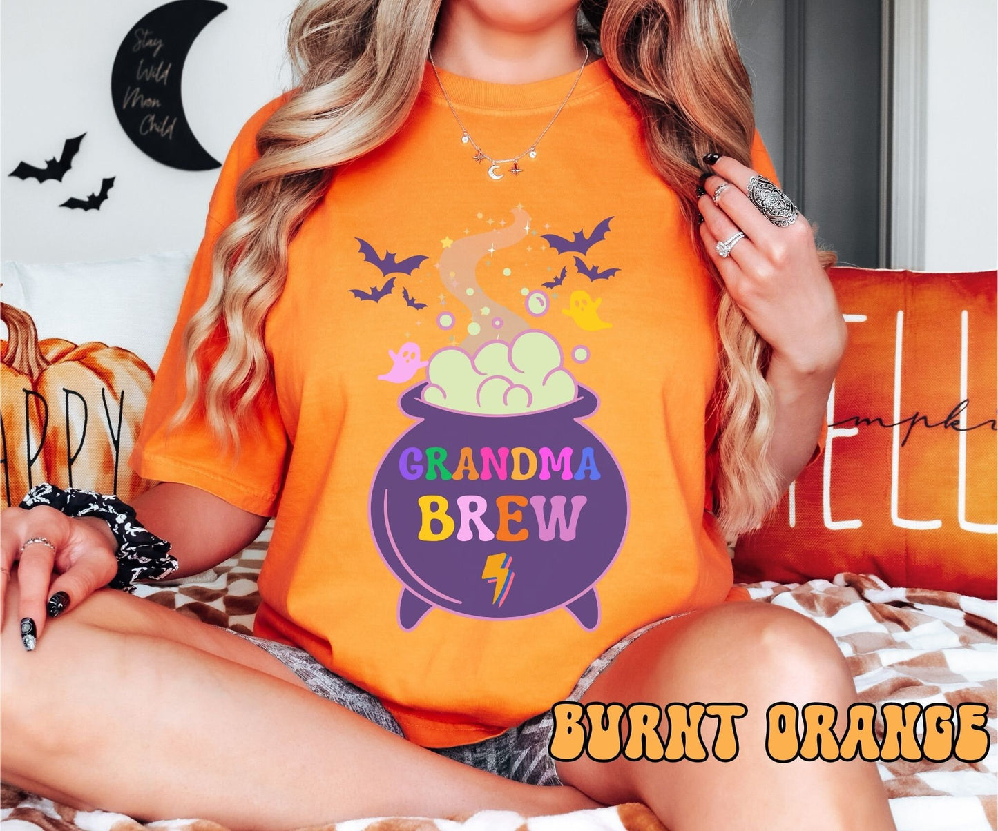 A shirt with a witch’s cauldron pouring out smoke with bats and ghosts in the air. The cauldron has text that says Grandma Brew