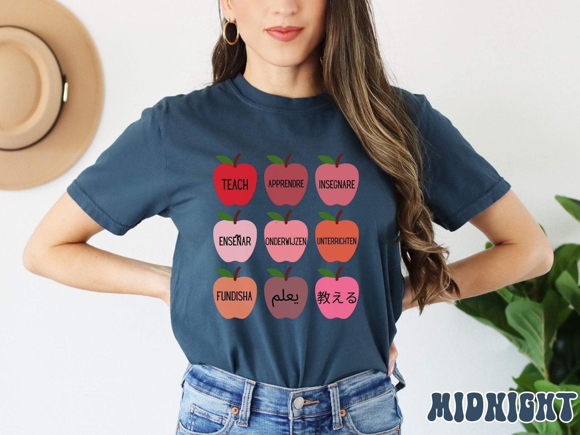 A woman wearing a vintage, midnight colored shirt with red, salmon, pink and orange colored apples with different variations of the word Teach in English, Spanish, French, German, Dutch, Arabic, Swahili, and Chinese.