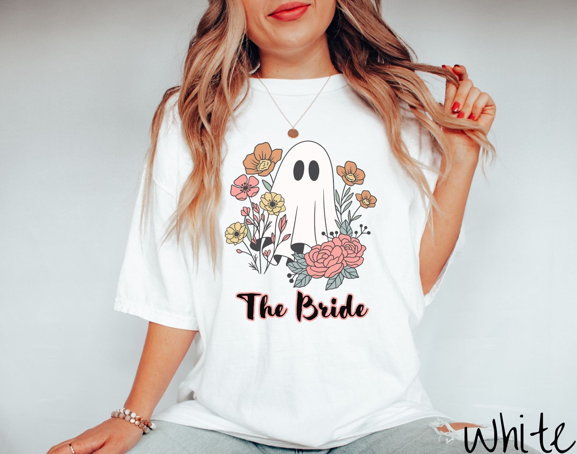 A woman wearing a cute white colored shirt with the text Boo Crew under a ghost figure holding a camera.