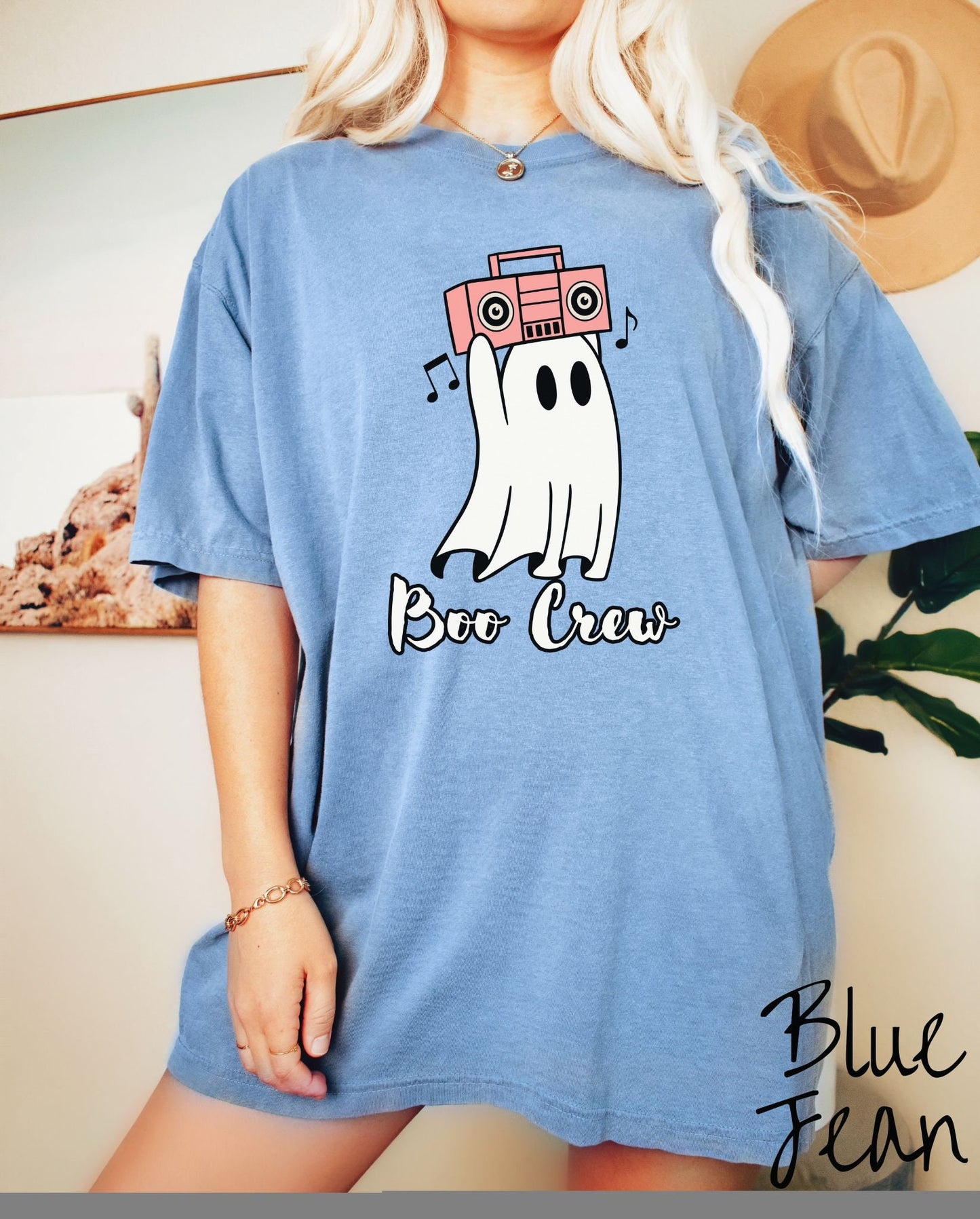 A woman wearing a cute blue jean colored shirt with the text Boo Crew under a ghost figure holding a camera.