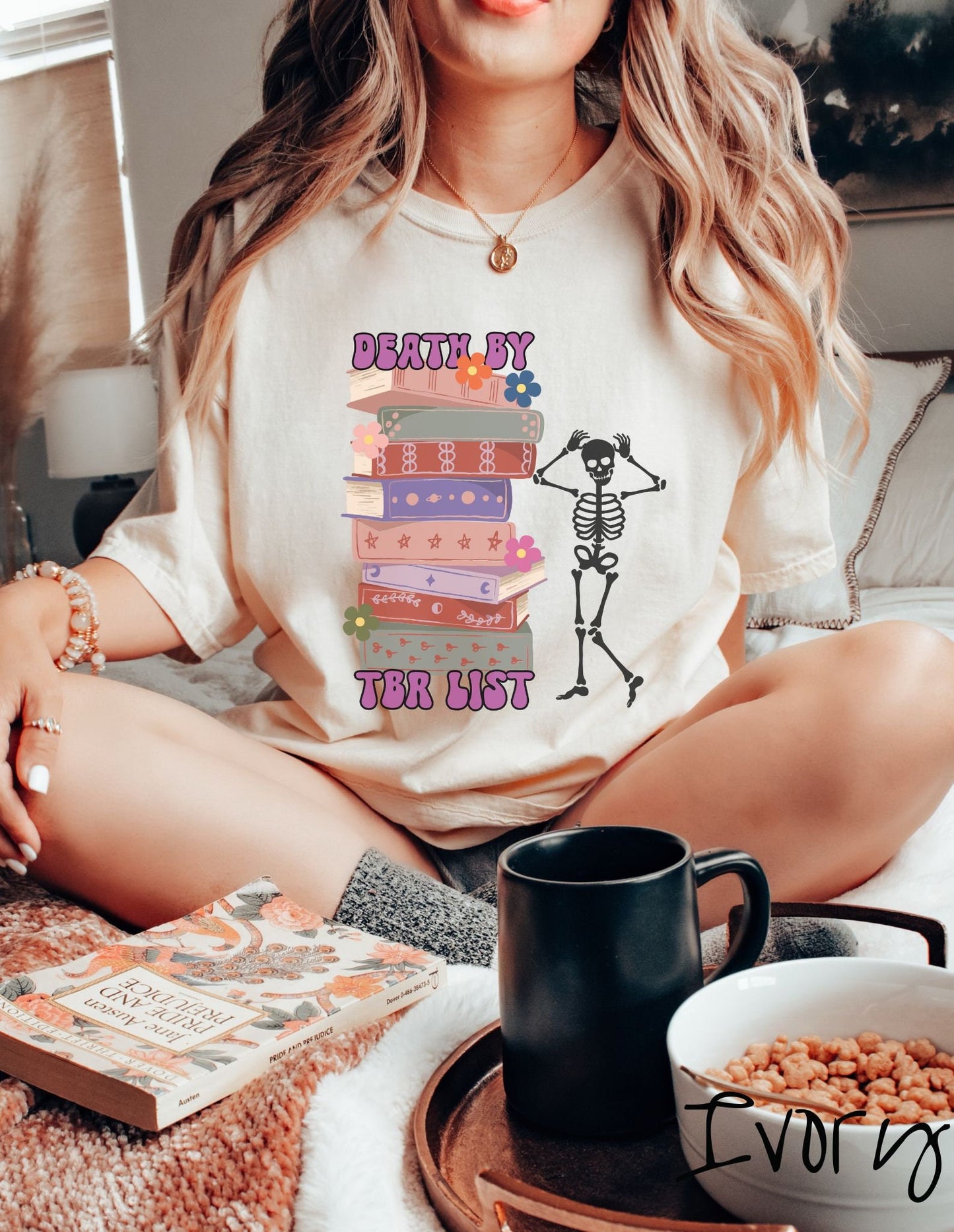 A woman wearing a cute ivory colored shirt with a huge stack of books with flowers sandwiched by the text Death by TBR List and a skeleton standing next to the stack with its hands on its head.