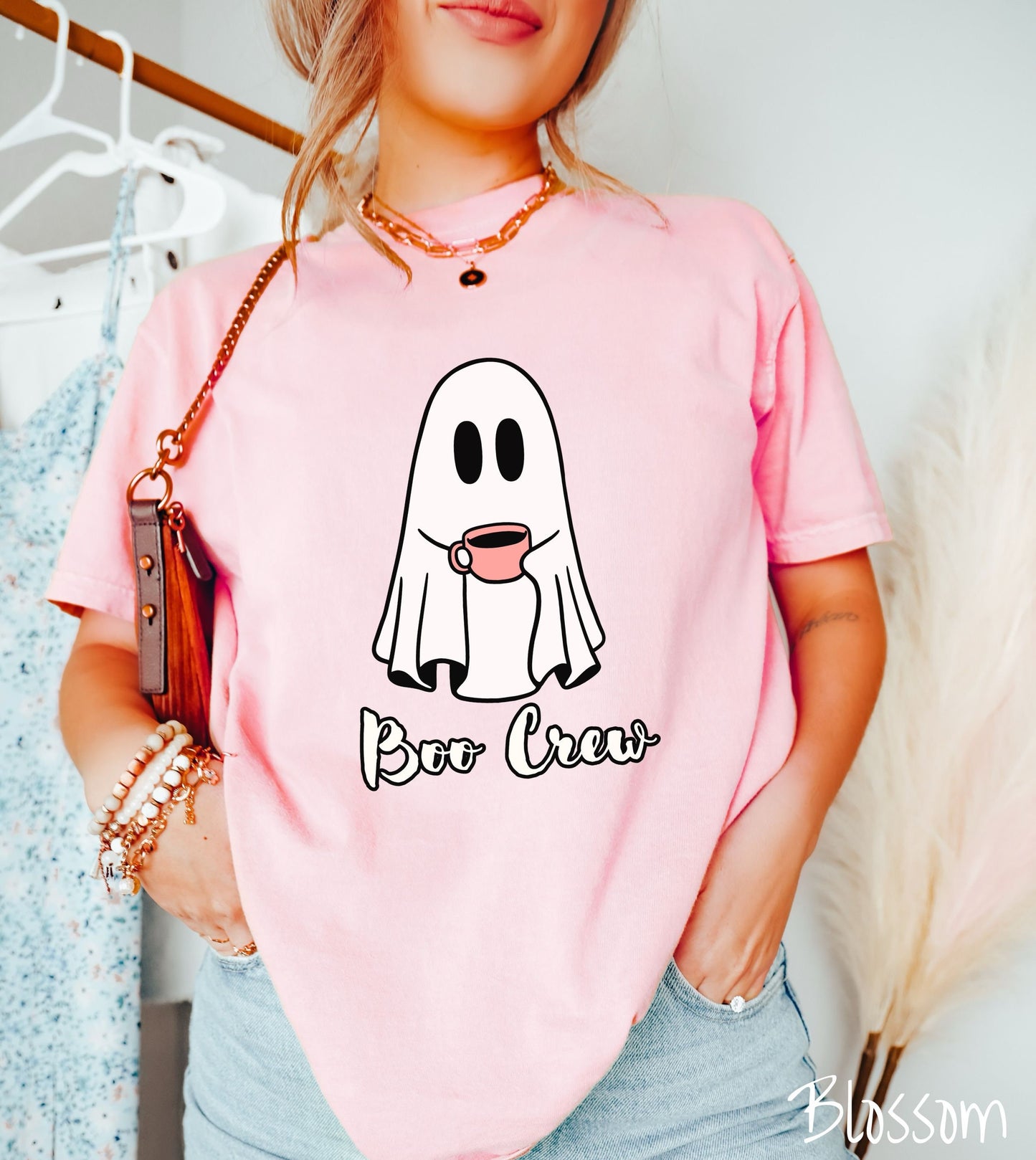 A woman wearing a cute blossom colored shirt with the text Boo Crew under a ghost figure holding a camera.