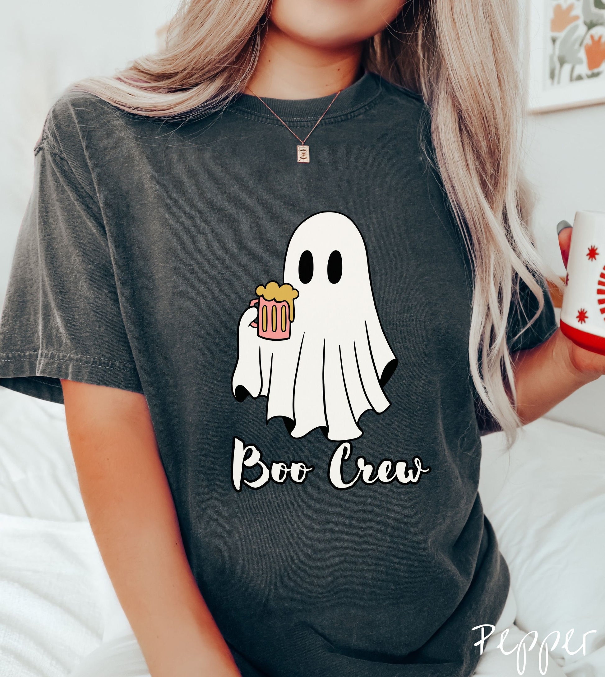 A woman wearing a cute pepper colored shirt with the text Boo Crew under a ghost figure holding a camera.