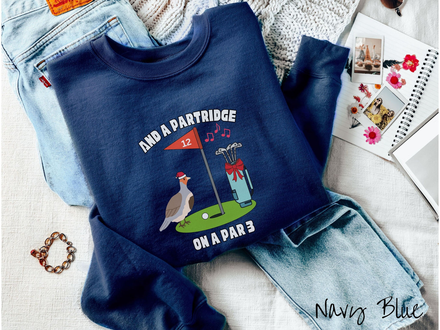 A cute navy blue colored sweatshirt with a partridge bird on a golf green next to a hole with a flag in it with #12 on it. There is also a set of golf clubs with a red bow and music playing in the air.
