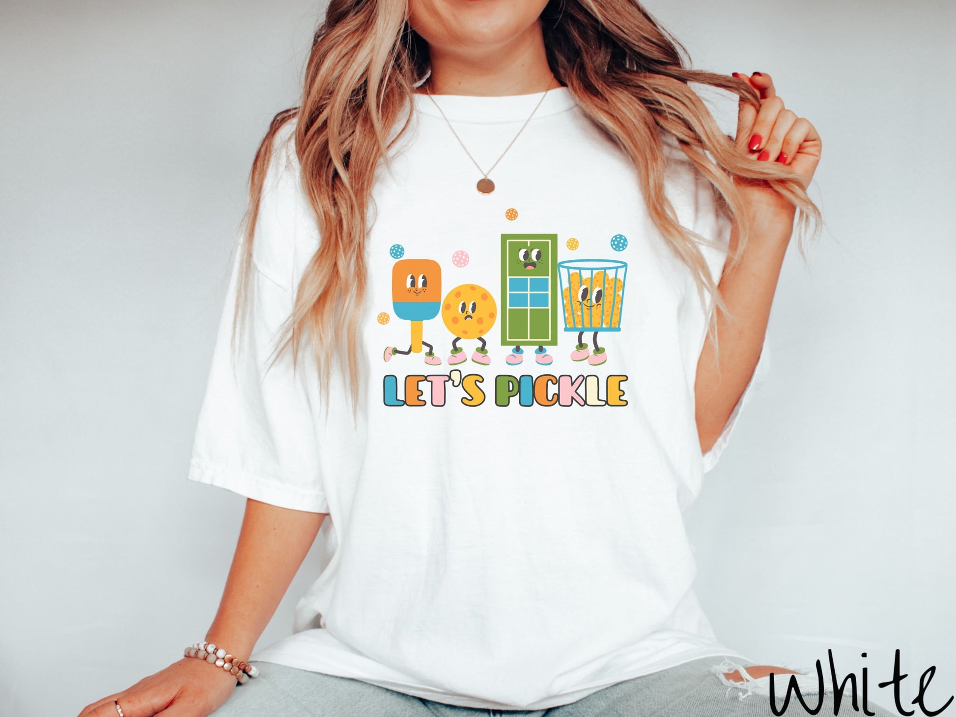 A woman wearing a cute white colored shirt with the text Let&#39;s Pickle along the bottom, and above the text are a popsicle, cookie, popcorn, and pickle balls.