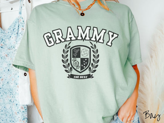 A woman wearing a cute bay colored shirt with text saying Grammy across the front with a varsity logo underneath with the words The Best centered underneath the logo.