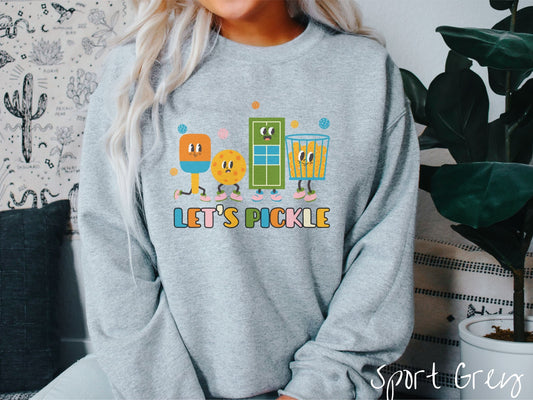 A woman wearing a cute sport grey colored sweatshirt with the text Lets Pickle, and above the text are a popsicle, cookie, popcorn, and pickle balls.