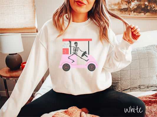 A woman wearing a cute white colored sweatshirt with a skeleton wearing a Santa hat driving a pink golf cart and waving.