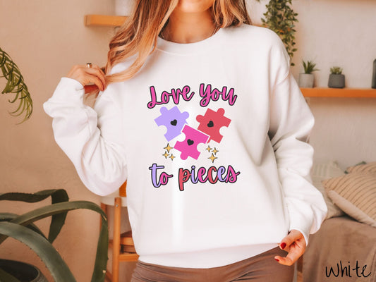 A woman wearing a cute, vintage white colored sweatshirt with the text Love you to pieces in red, pink, and purple colors, and three red, pink, and purple puzzle pieces with hearts on them surrounded by yellow stars.