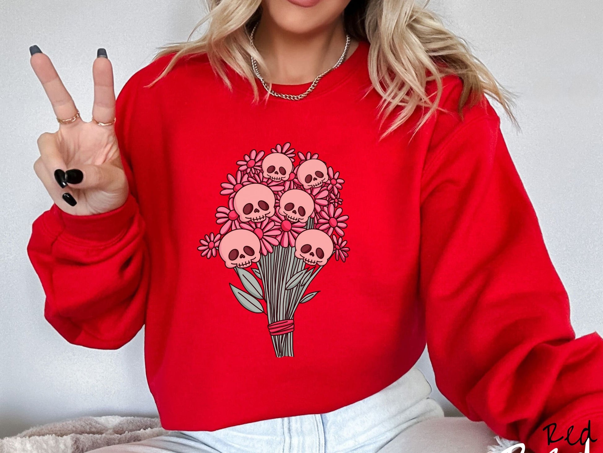A woman wearing a cute red colored sweatshirt with a spooky flower bouquet with skull heads as the flowers among pink colored flowers.