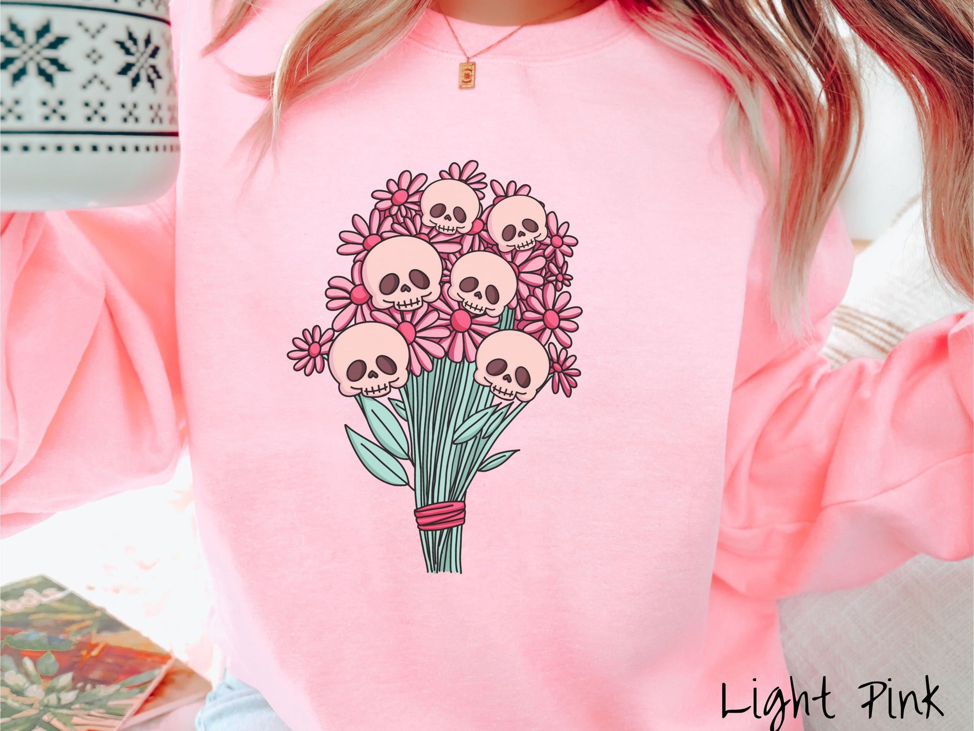 A woman wearing a cute light pink colored sweatshirt with a spooky flower bouquet with skull heads as the flowers among pink colored flowers.