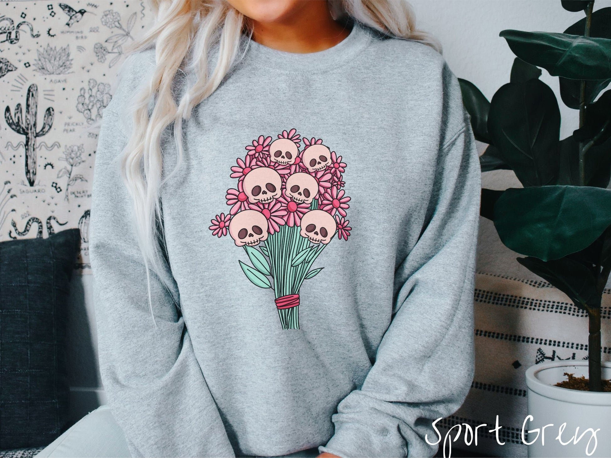 A woman wearing a cute sport grey colored sweatshirt with a spooky flower bouquet with skull heads as the flowers among pink colored flowers.