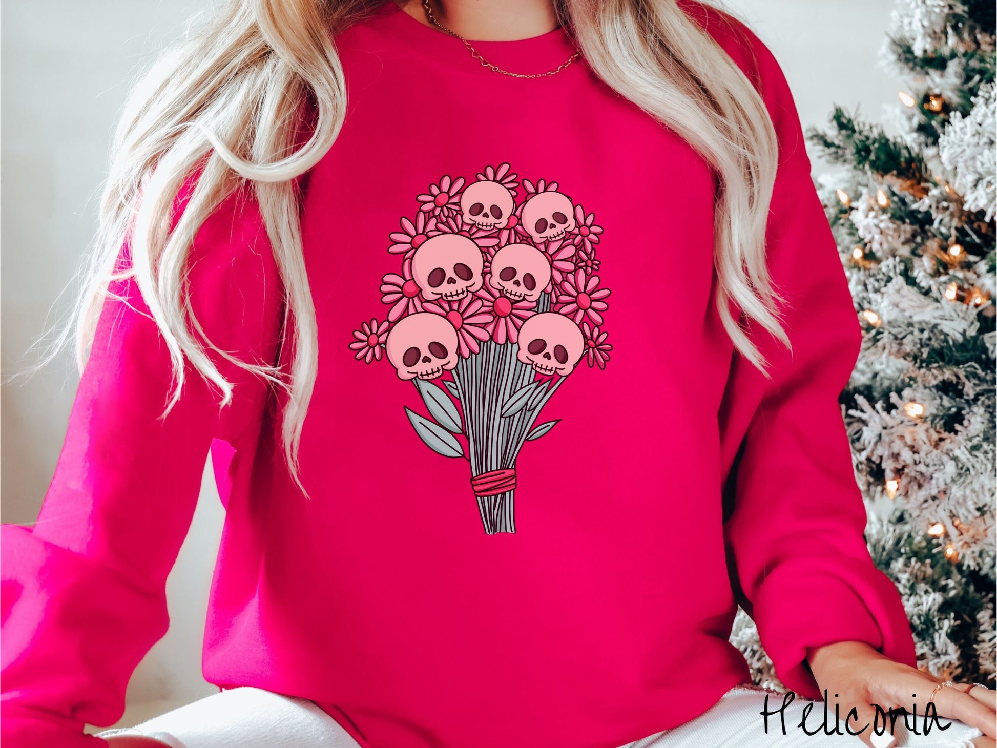 A woman wearing a cute heliconia colored sweatshirt with a spooky flower bouquet with skull heads as the flowers among pink colored flowers.
