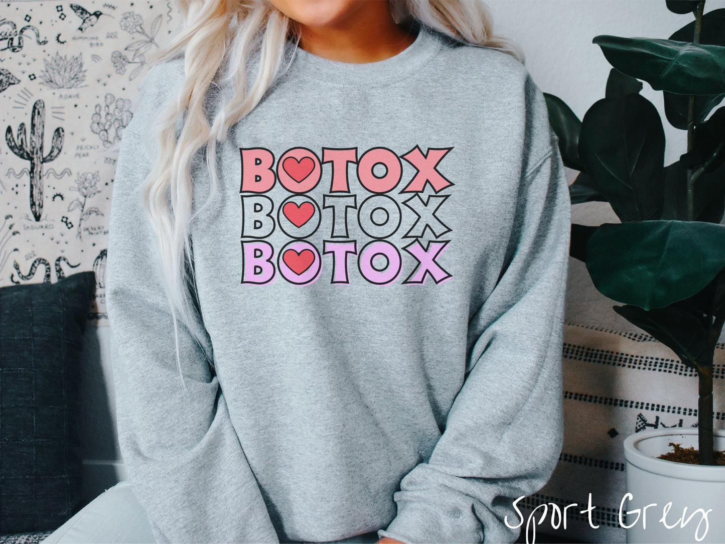 A woman wearing a cute sport grey colored sweatshirt with the word Botox listed three times in different shades of pink and red, with red hearts inside the first letter O in Botox.