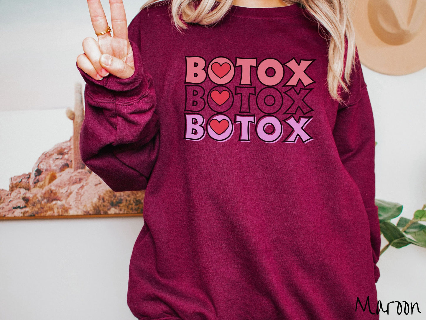 A woman wearing a cute maroon colored sweatshirt with the word Botox listed three times in different shades of pink and red, with red hearts inside the first letter O in Botox.