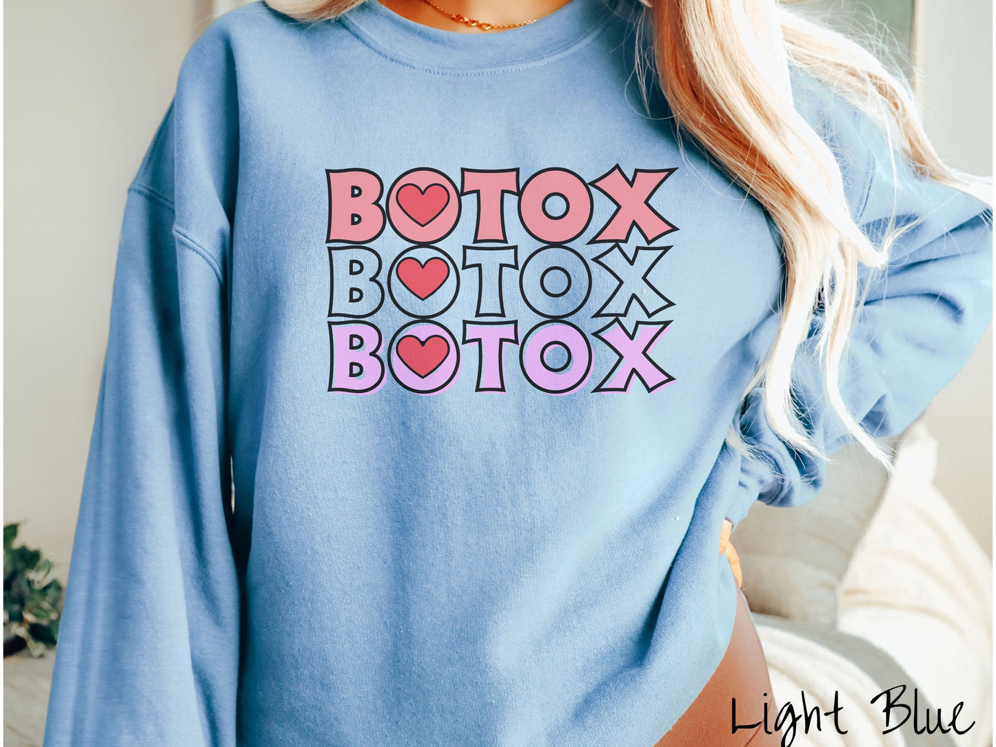 A woman wearing a cute light blue colored sweatshirt with the word Botox listed three times in different shades of pink and red, with red hearts inside the first letter O in Botox.