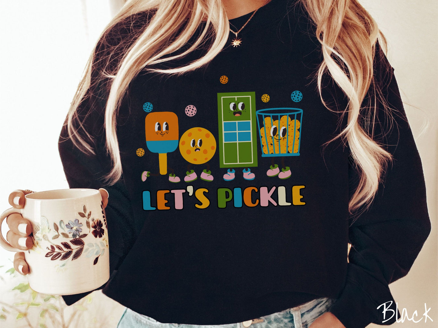 A woman wearing a cute black colored sweatshirt with the text Lets Pickle, and above the text are a popsicle, cookie, popcorn, and pickle balls.