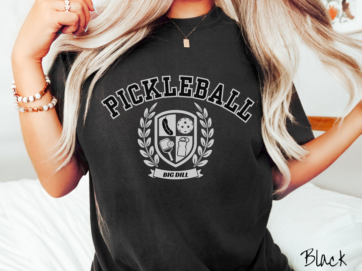 A woman wearing a cute black colored shirt with the text Pickleball across the top, a varsity logo centered underneath, and the words Big Dill underneath the logo.