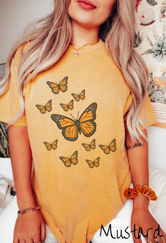 A woman wearing a vintage, mustard colored shirt with a large yellow and black butterfly in the center of the shirt and nine smaller yellow and black monarch butterflies fluttering around behind it.