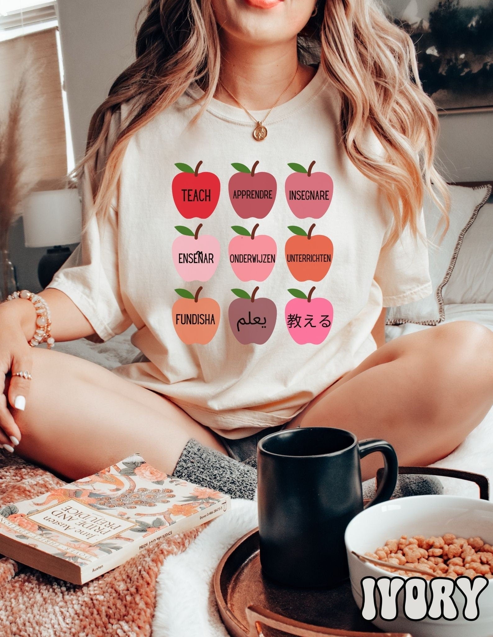 A woman wearing a vintage, ivory colored shirt with red, salmon, pink and orange colored apples with different variations of the word Teach in English, Spanish, French, German, Dutch, Arabic, Swahili, and Chinese.