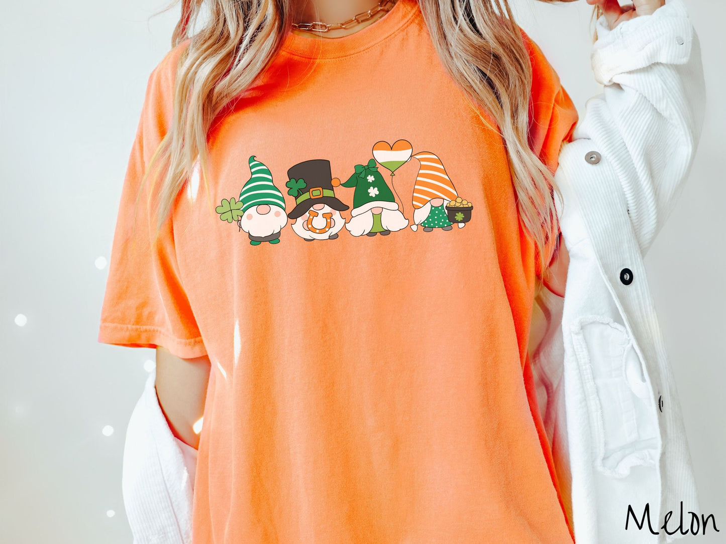 A woman wearing a vintage, melon colored shirt with four festive gnomes wearing varying green, white, and orange hats holding a green clover, an inflatable balloon, an orange horse shoe, and a pot of gold.