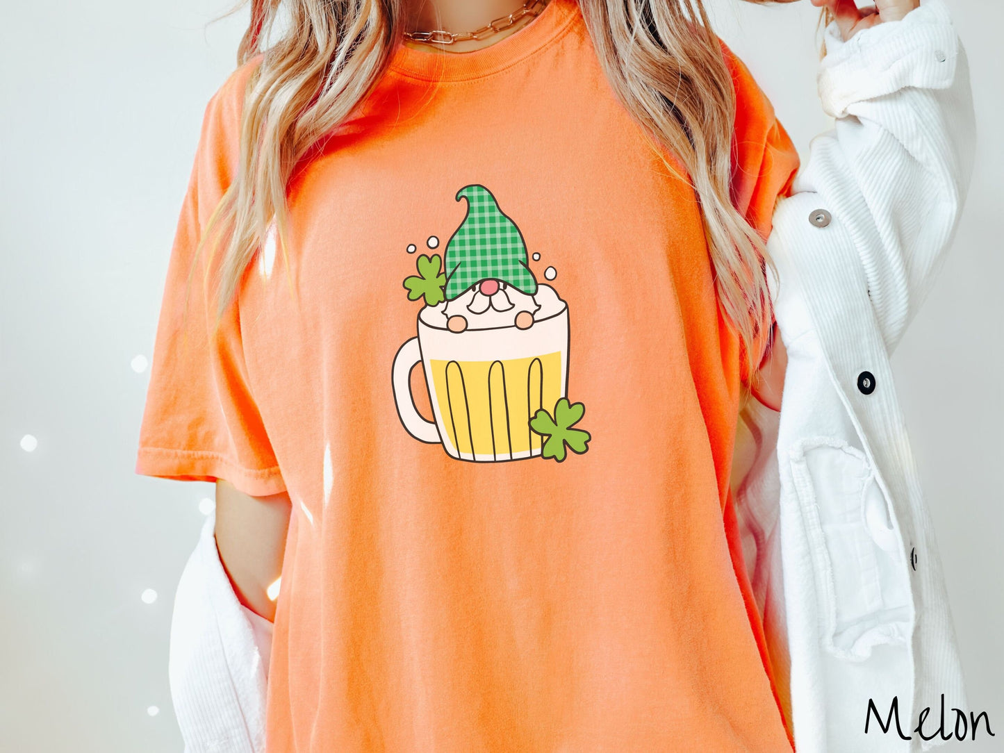 A woman wearing a vintage, melon colored shirt with a beer filled mug in the center with a green hat wearing gnome peeking over the top of the glass and green clovers in the background.