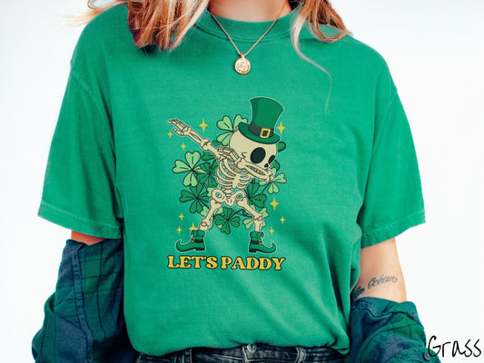 A woman wearing a vintage, grass colored shirt with the text Lets Paddy and above that is a leprechaun wearing a green top hat and green elf shoes doing the dab dance and there are green clovers and golden stars in the background.