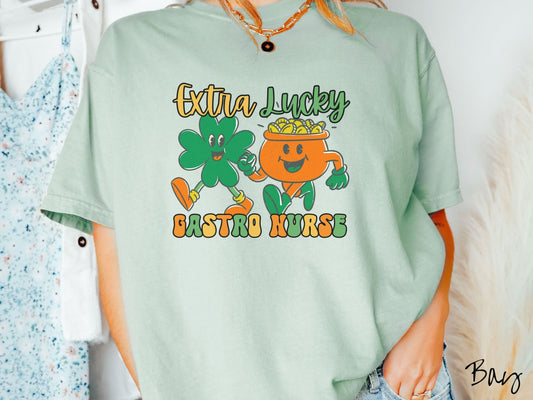 A woman wearing a vintage, bay colored shirt with the text Extra Lucky Gastro Nurse in yellow, orange, and green font. Between the text are a green clover and orange pot of gold smiling and walking together in step.