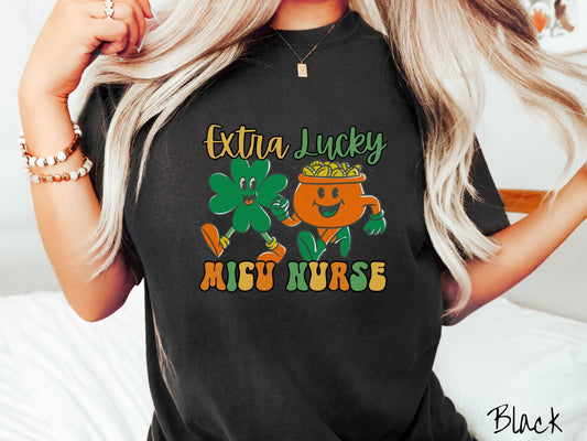 A woman wearing a vintage, black colored shirt with the text Extra Lucky MICU Nurse  in yellow, orange, and green font. Between the text are a green clover and orange pot of gold smiling and walking together in step.