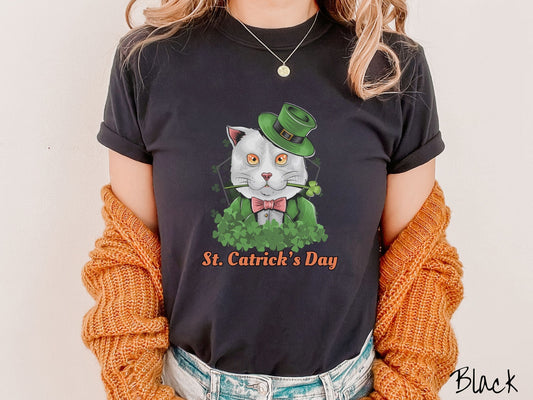 A woman wearing a vintage, black colored shirt with a white cat with yellow and orange eyes and a green three leaf clover in its mouth, a pink bowtie, a green top hat and green suit smiling and the text St. Catricks Day below it.