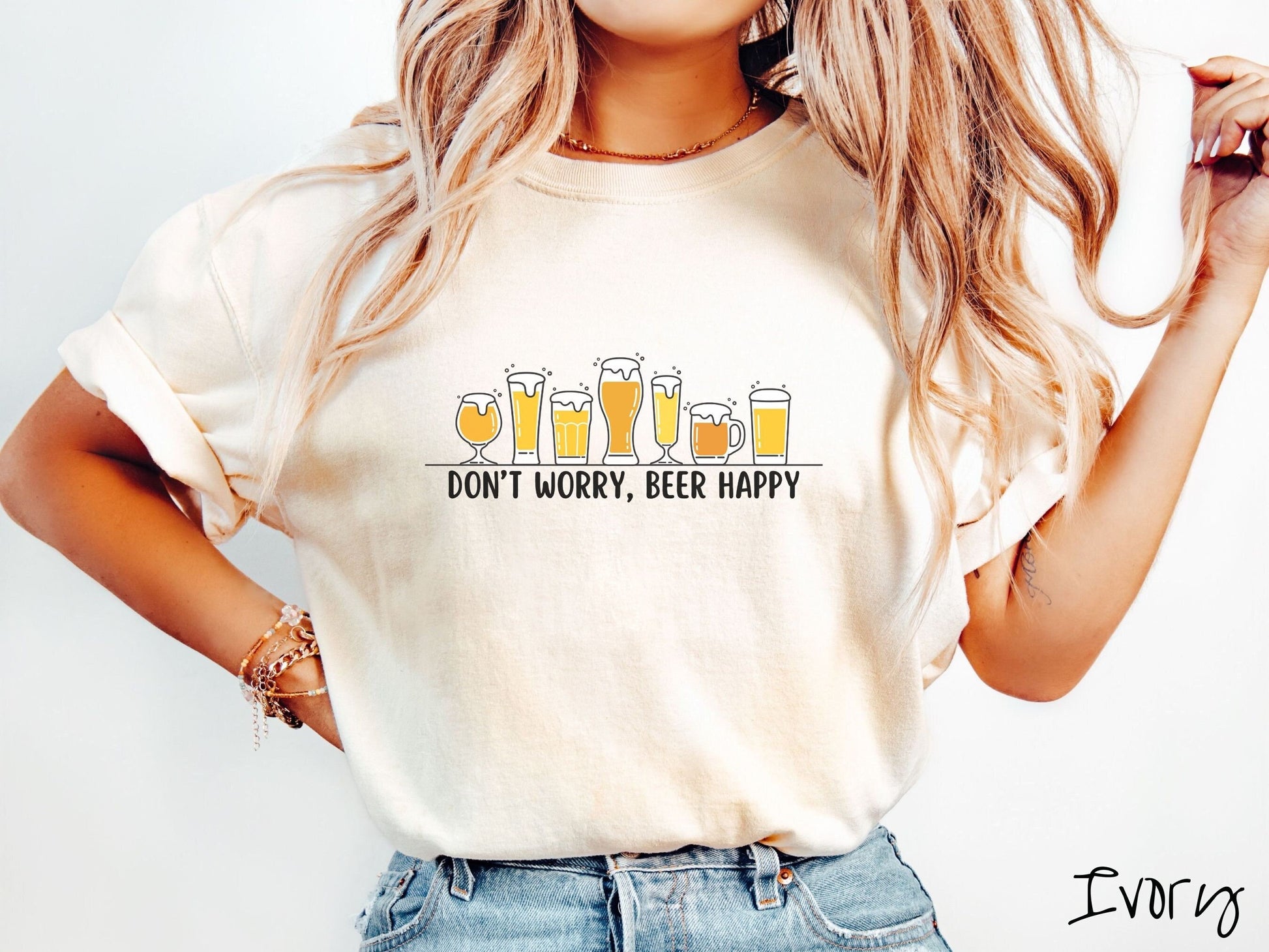 A woman wearing a vintage, ivory colored shirt with the text Dont Worry, Beer happy, and above this are varying sizes and shapes of beer glasses with yellow and orange ber all of them have foam coming out the tops.