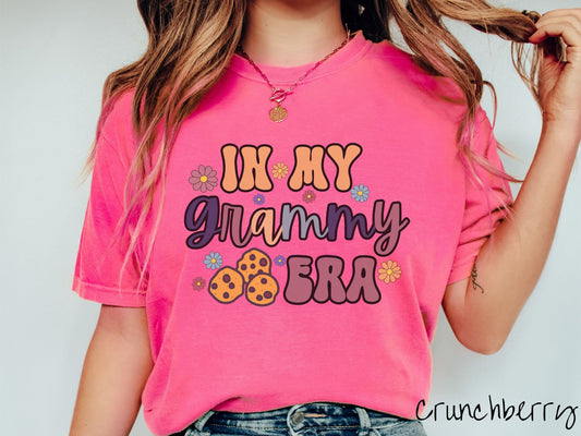 A woman wearing a cute, pink shirt with the text saying In My Grammy era with flowers and chocolate chip cookies mixed within the text.