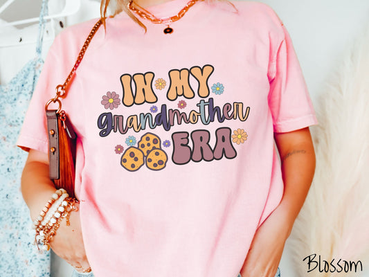 A woman wearing a cute blossom colored shirt with text on the front saying In My Grandmother Era, with flowers and chocolate chip cookies mixed within the text.