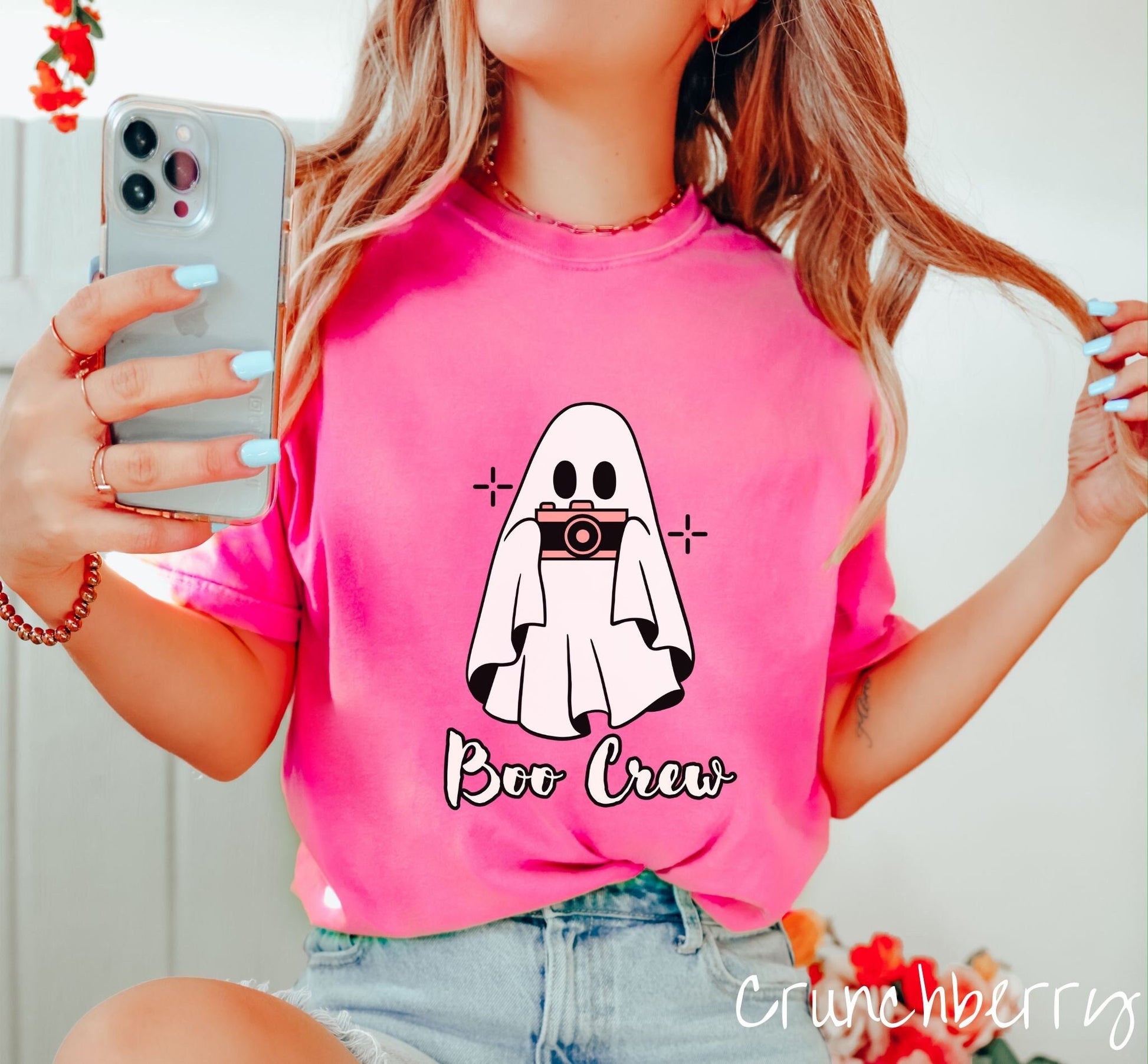 A woman wearing a cute crunchberry colored shirt with the text Boo Crew under a ghost figure holding a camera.