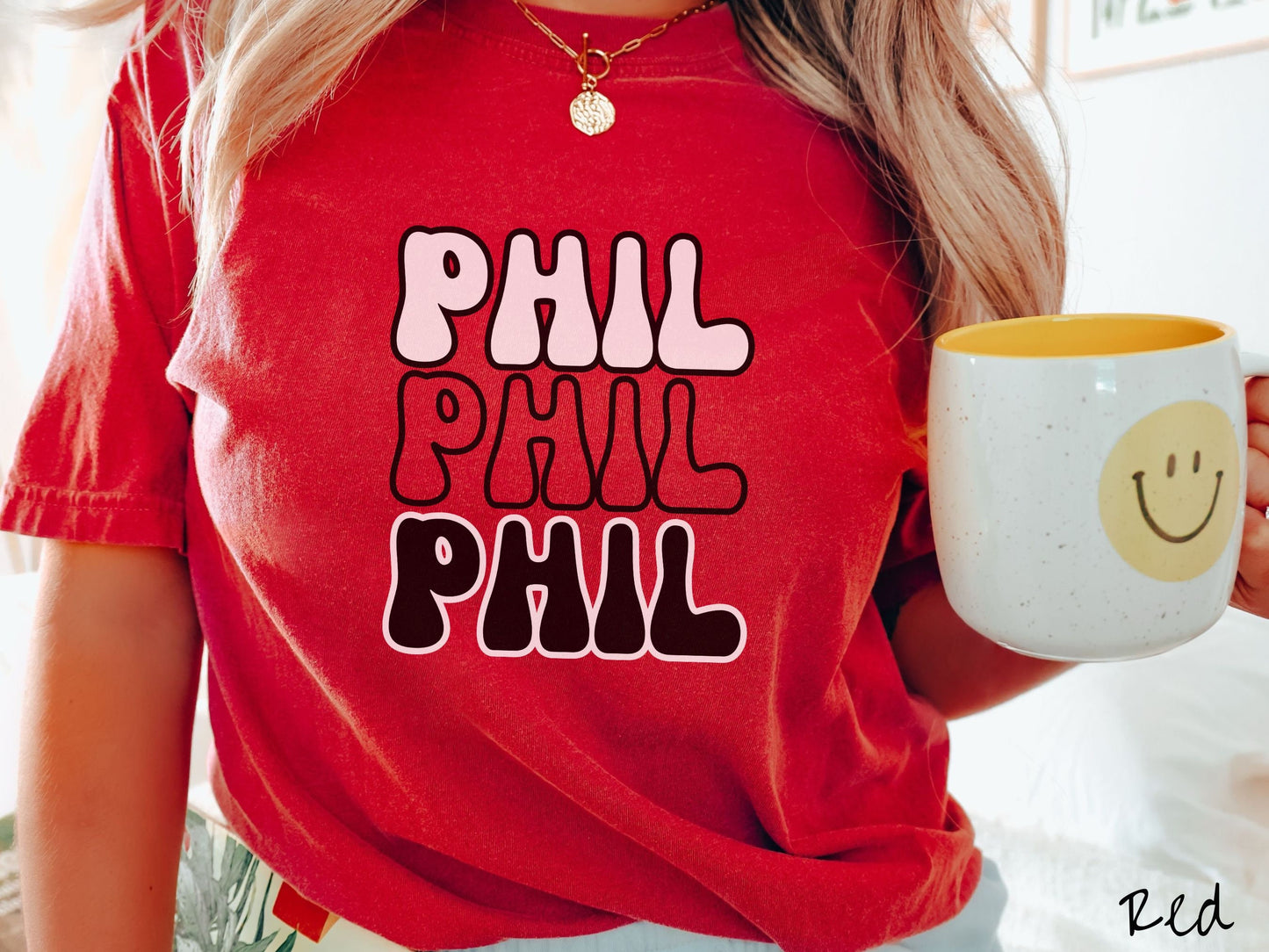 A woman wearing a cute red colored shirt with the text PHIL listed three times vertically in white, red, and black color text. The shirt is referring to the chant that occurs for the groundhog Phil every Groundhogs Day in Punxsutawney, PA.
