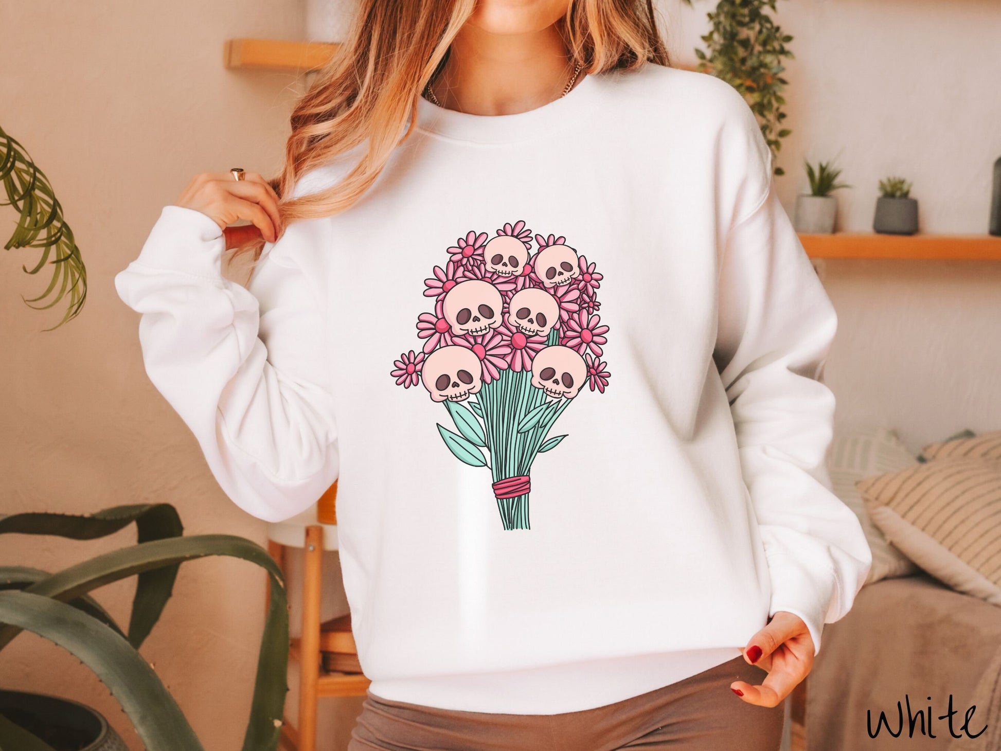 A woman wearing a cute white colored sweatshirt with a spooky flower bouquet with skull heads as the flowers among pink colored flowers.