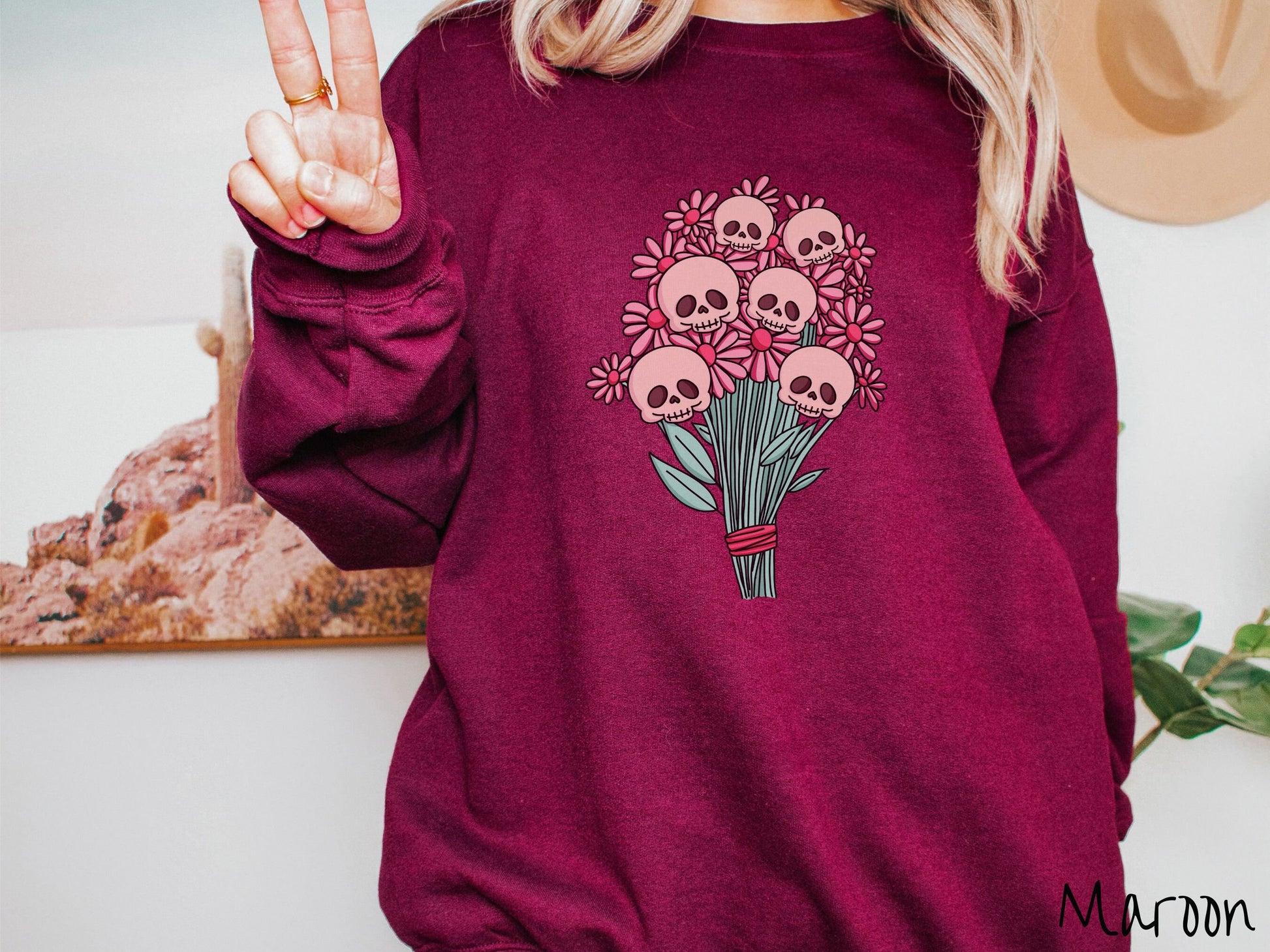 A woman wearing a cute maroon colored sweatshirt with a spooky flower bouquet with skull heads as the flowers among pink colored flowers.
