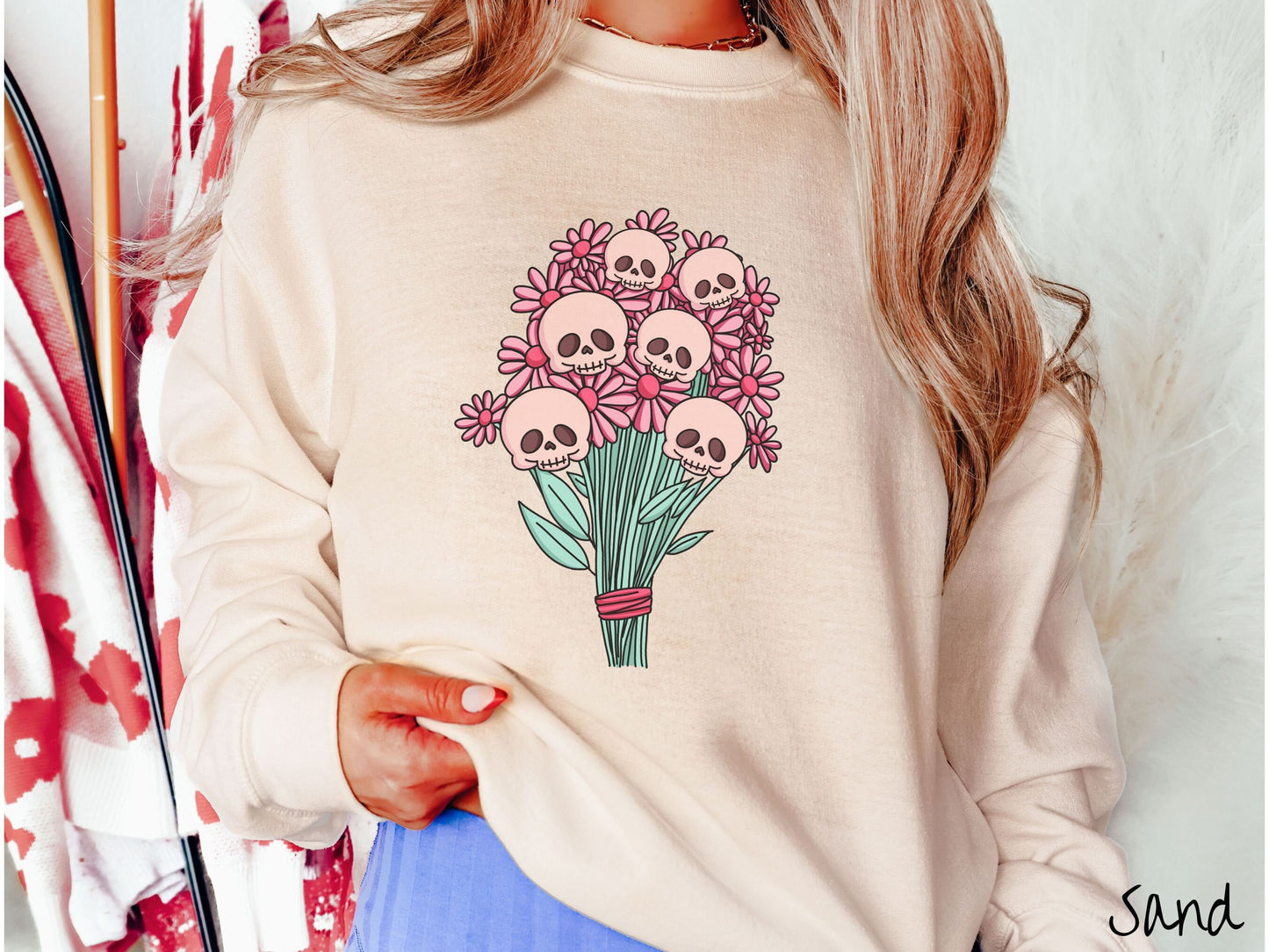 A woman wearing a cute sand colored sweatshirt with a spooky flower bouquet with skull heads as the flowers among pink colored flowers.