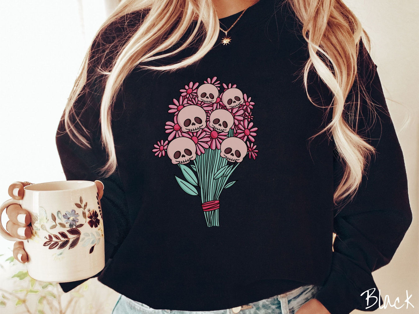A woman wearing a cute black colored sweatshirt with a spooky flower bouquet with skull heads as the flowers among pink colored flowers.
