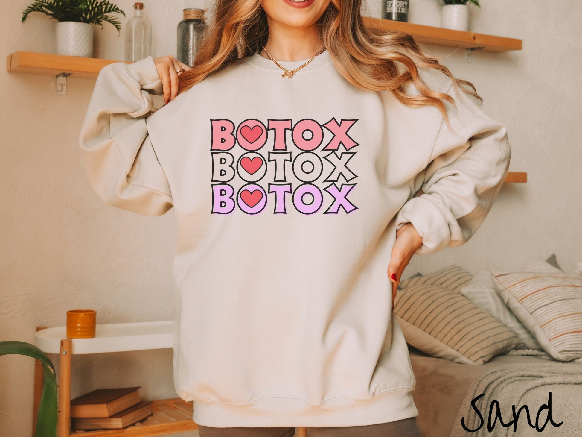 A woman wearing a cute sand colored sweatshirt with the word Botox listed three times in different shades of pink and red, with red hearts inside the first letter O in Botox.