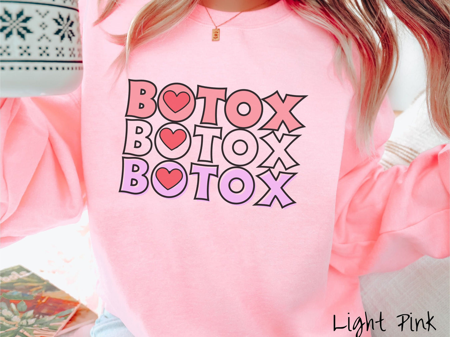 A woman wearing a cute light pink colored sweatshirt with the word Botox listed three times in different shades of pink and red, with red hearts inside the first letter O in Botox.