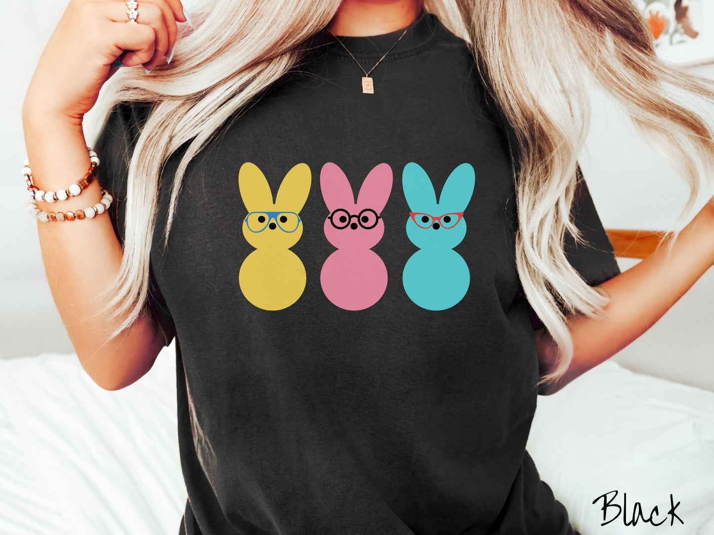A woman wearing a cute, vintage black colored shirt with three peep-like rabbits on the front. One is yellow and wearing blue glasses, the middle is pink with black glasses, and the one on the right is light blue with red glasses.