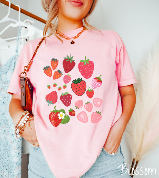 A woman wearing a vintage, blossom colored shirt with many different sizes and colors of strawberries, colors include light red, red, dark red, pink, and blossom.